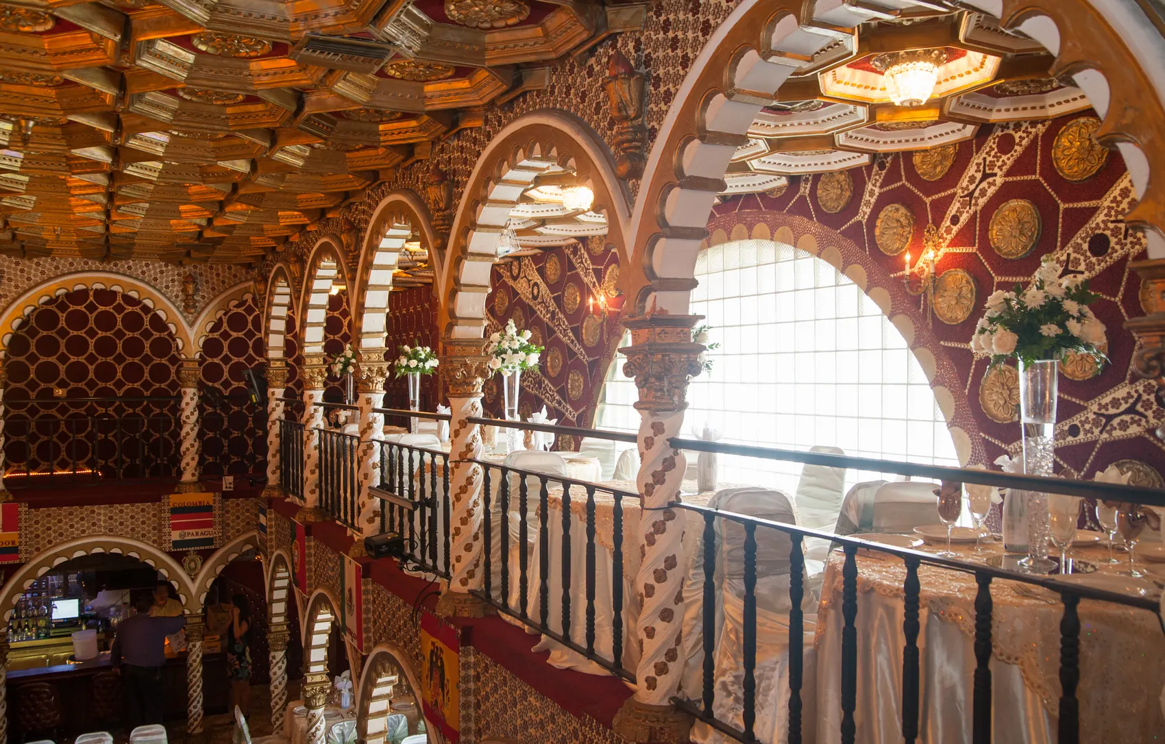 The upper balcony beside a tall arched window, banquet tables and flowers below.