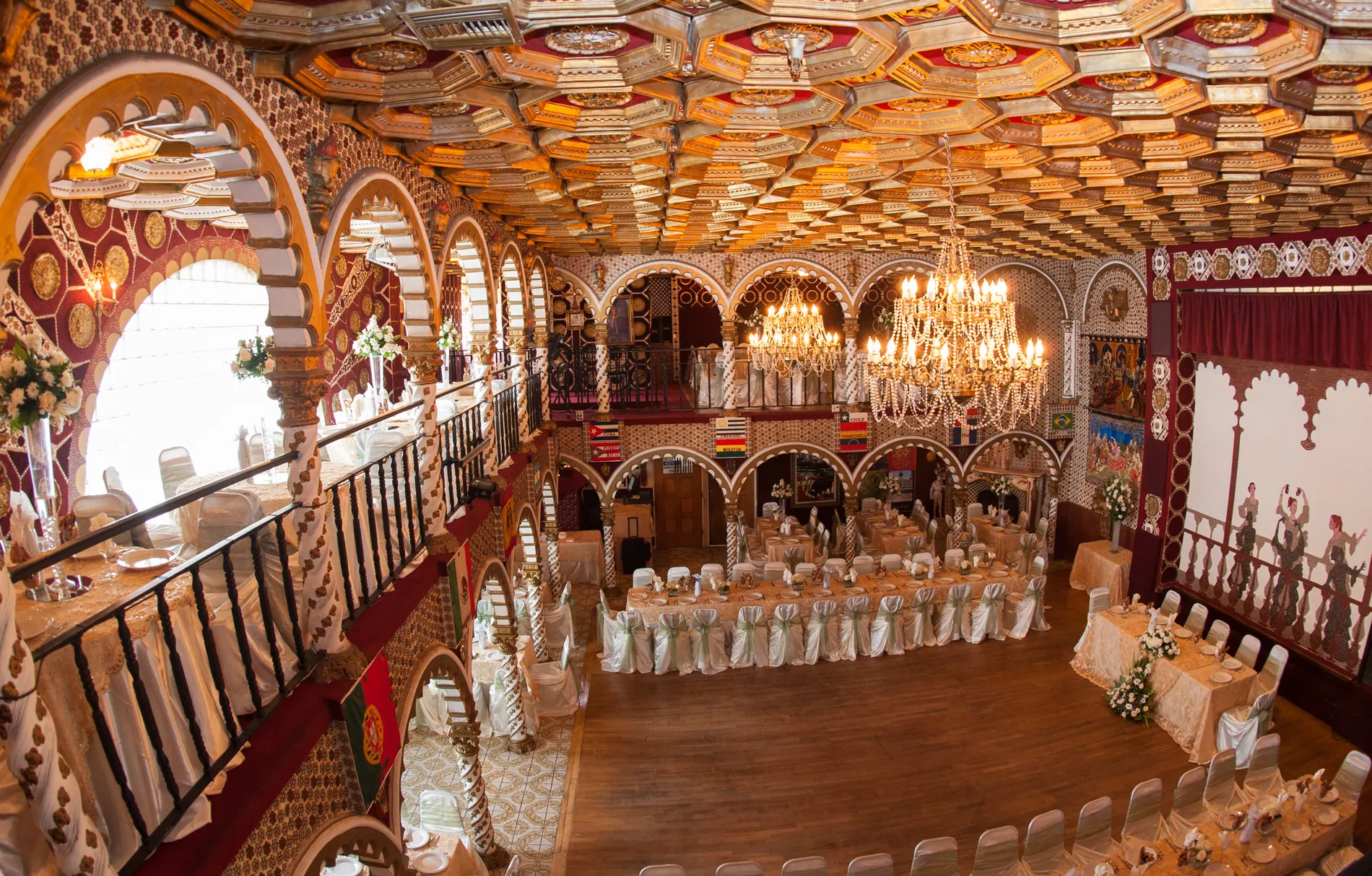 The ballroom from the upper balcony: a chandelier over two levels of arches and a full banquet below.