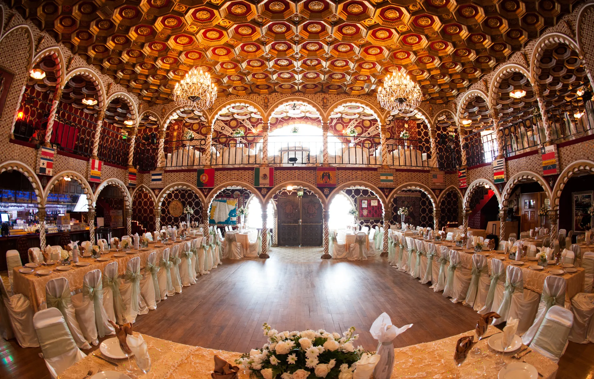 The Moorish ballroom seen head-on: twin chandeliers, a honeycomb ceiling, arched balconies, and a wood dance floor ringed by banquet tables.