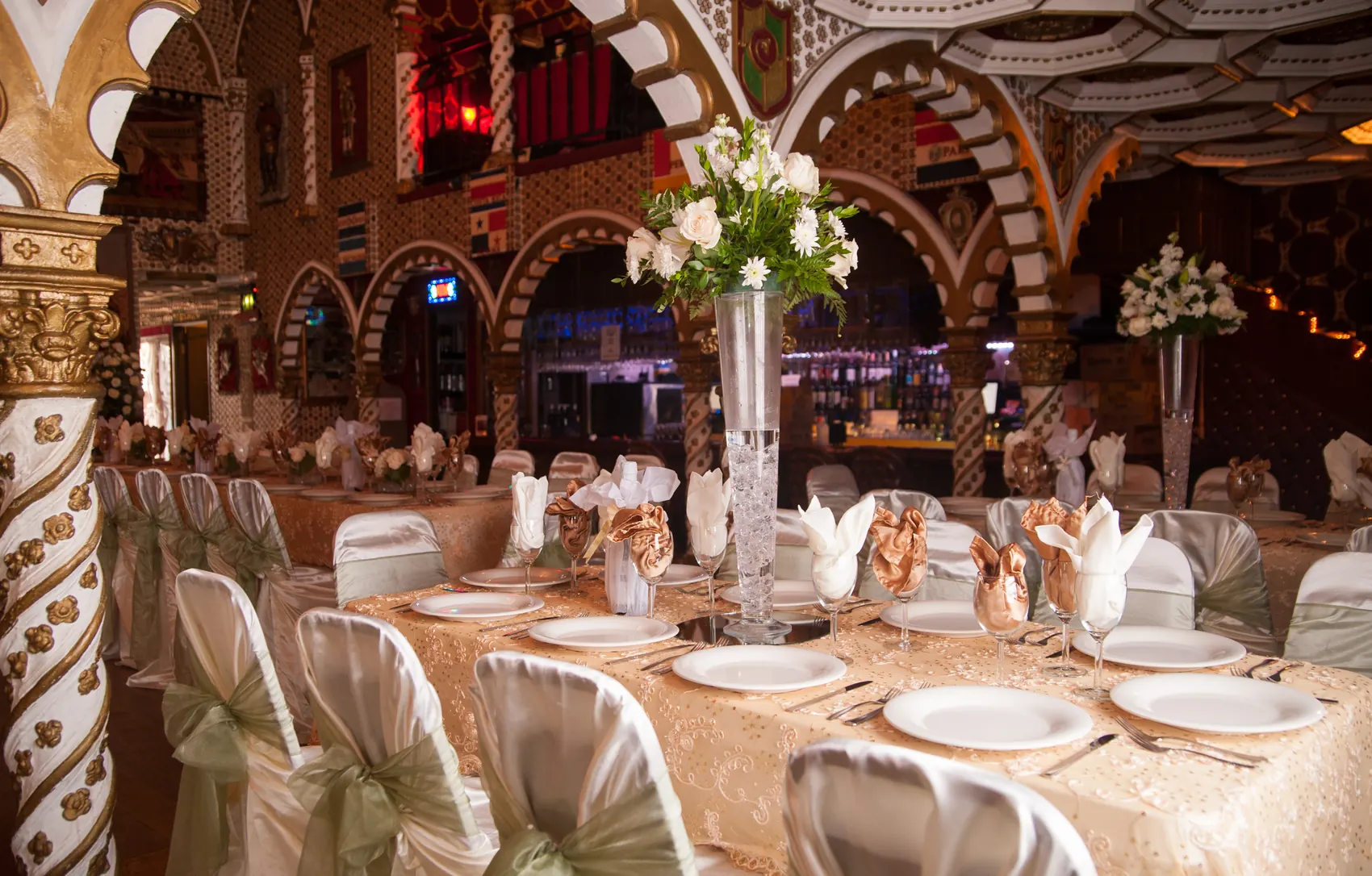 Banquet tables with tall floral centerpieces set beneath the arches for an evening event.