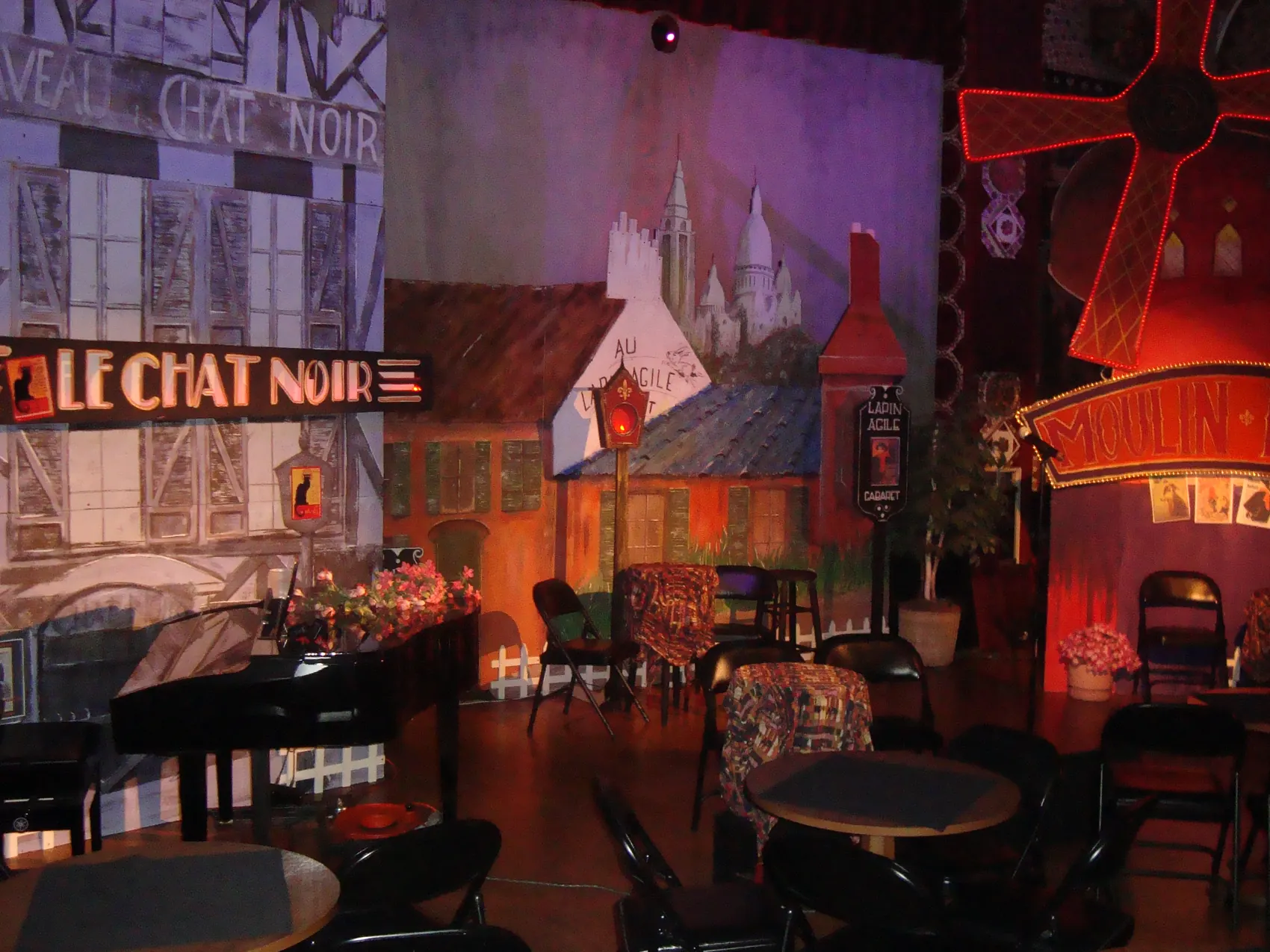 A grand piano on a Parisian cabaret stage set painted with a Le Chat Noir street scene.