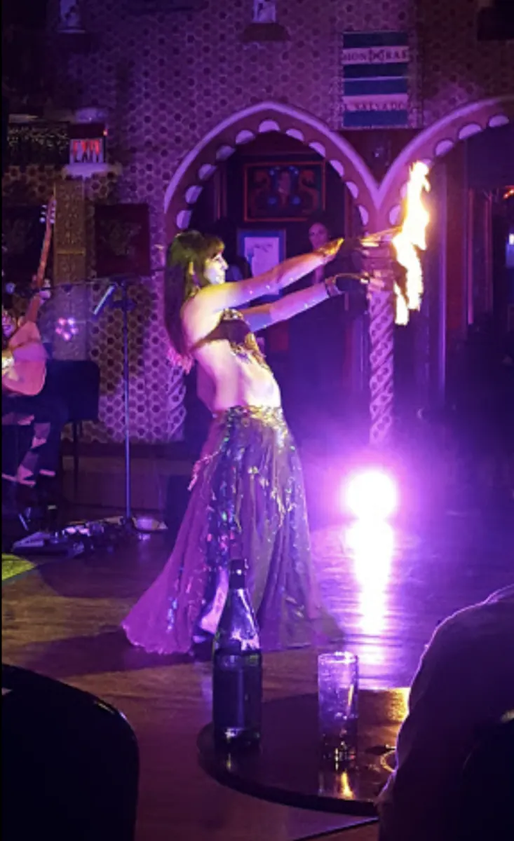 A performer with fire on stage under violet light.