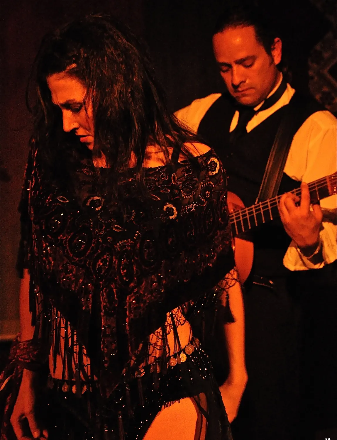 A flamenco couple posed close together under deep red light.