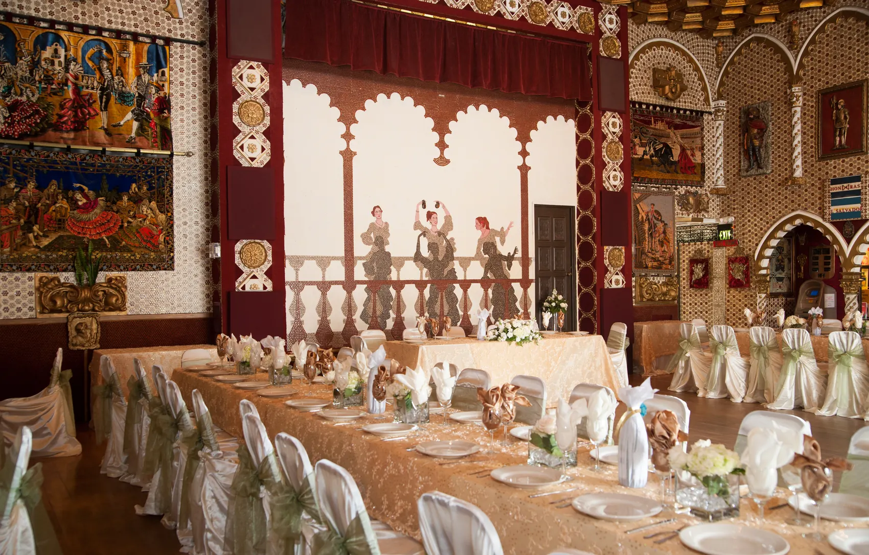 A long head table set with linen, framed by hand-cast relief figures of dancers on the wall behind.