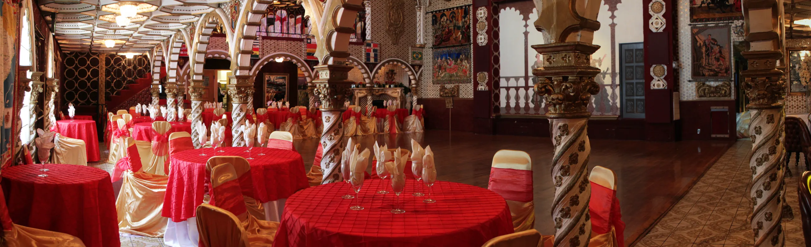 The ballroom set for a banquet, round tables dressed in red and gold beneath the arches and spiral columns.