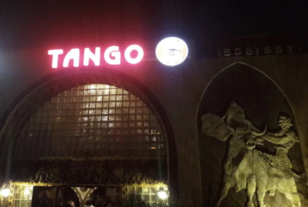 The red TANGO neon sign glowing at night beside a sculpted dancer relief on the facade.